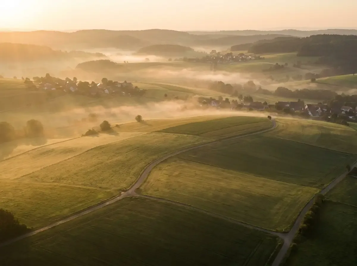 Morgennebel über einer weiten Hügellandschaft mit Feldern und kleinen Ortschaften